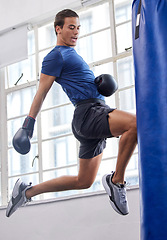 Image showing Gym, jump and kick of boxer man for sports workout, training and athlete practice with equipment. Energy, focus and strength of martial arts fighter at kickboxing fitness club with punching bag.