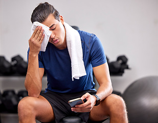 Image showing Sweat, tired and man resting in the gym after a intense workout, exercise sports training. Fitness, sport and male athlete networking on social media with a phone after exercising in wellness studio.