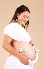 Image showing Pregnant, mother and flowers on stomach, healthcare and excited for birth, smile and girl on brown studio background. Pregnancy, woman and mama with tummy, plants and nurture for wellness and growth