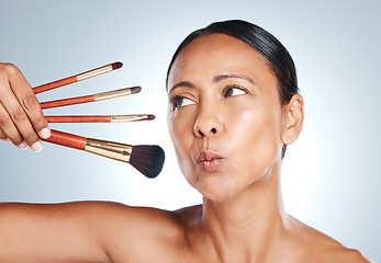 Image showing Face, beauty and senior woman with makeup brushes in studio isolated on a gray background. Cosmetics, skincare products and mature female model pout lips with tools to apply foundation and powder.