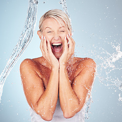 Image showing Skincare, excited and portrait of a woman with a water splash isolated on a blue background. Self care, happy and face of an elderly beauty model cleaning her body for wellness on a studio backdrop