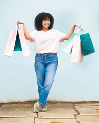 Image showing Shopping, excited and portrait of a woman with bags from a sale on a blue city wall in Greece. Fashion, product and girl shopper carrying content from a shop, boutique or store downtown with a smile