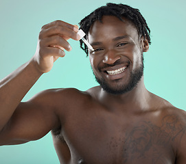 Image showing Man, face portrait and oil with dropper for skincare, beauty and self care in studio. Healthy and happy black person on blue background for facial serum, dermatology and cosmetic product for skin