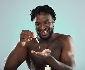 Image showing Man, face serum and happy about skincare, beauty and self care product in studio. Healthy black person on blue background for facial oil, dermatology and cosmetics for skin glow, health and wellness