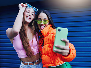 Image showing Fashion, selfie and friends with phone on blue background with style, cool sunglasses and urban clothes. Social media, smartphone and women smile for photo on weekend, vacation and holiday in city