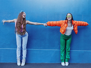 Image showing Friends, wall and city for fashion with girl, holding hands and outdoor for funny, comic face or happy together. Gen z women, metro and blue background for trendy clothes, sneakers or urban adventure