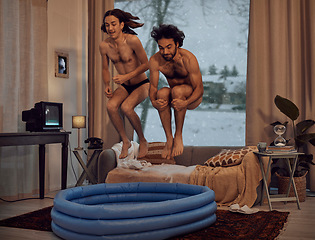 Image showing Hipster, rebel and jump into inflatable pool in a lounge inside a retro home or house having fun and playing. Funny, snow and men dive together in the living room for a winter vacation or holiday