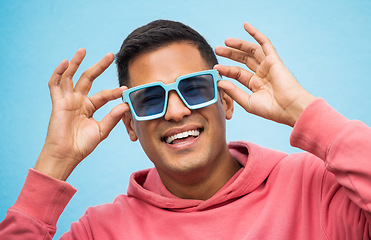 Image showing Happy, man with sunglasses and smile with face, trendy fashion and happiness with freedom isolated on blue background. Funky, retro and wellness, hipster person in studio with vintage designer brand