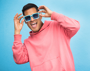 Image showing Happiness, man with sunglasses and smile with face, trendy fashion and happy with freedom isolated on blue background. Funky, retro and wellness, hipster person in studio with vintage designer brand