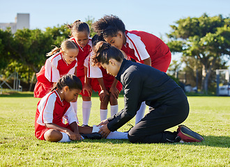 Image showing Accident, injury and children soccer team with their coach in a huddle helping a girl athlete. Sports, first aid and kid with a sore, pain or muscle sprain after a match on an outdoor football field.