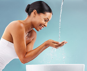 Image showing Black woman, cleaning and water splash on blue background for skincare, wellness and beauty. Happy model, facial shower drops and washing basin in bathroom studio for aesthetic, cosmetics and smile