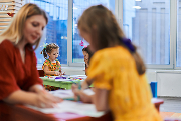 Image showing Creative kids during an art class in a daycare center or elementary school classroom drawing with female teacher.