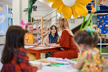 Image showing Creative kids during an art class in a daycare center or elementary school classroom drawing with female teacher.