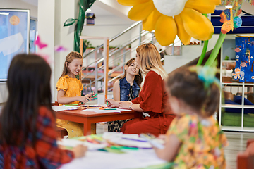 Image showing Creative kids during an art class in a daycare center or elementary school classroom drawing with female teacher.