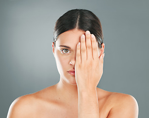 Image showing Face, cover and portrait of a woman with a hand on eye isolated on a grey studio background. Skincare, beauty and serious model hiding eyes for dermatology, botox problem and cosmetics on a backdrop