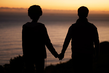 Image showing Sunset, beach and silhouette of couple holding hands for date by the sea with dark shadow, love and care. Horizon, ocean and people rear with together in nature for hiking or travel goals on holiday