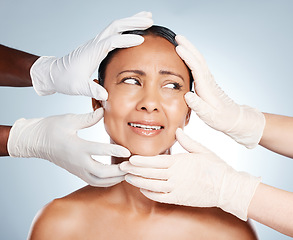 Image showing Plastic surgery, scared and face of woman with hands from doctors isolated on blue background. Skincare, check and senior person worried about botox, cosmetic and facial surgery with professionals