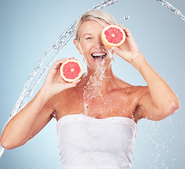 Image showing Woman, studio portrait and grapefruit with water splash, smile and happy for wellness by blue background. Senior model, organic citrus fruit and vitamin c for health, nutrition and self care process