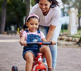 Image showing Mother, child and bicycle teaching with training wheels for learning or practice at the park. Happy mom helping little girl to ride her first bike with smile for proud playful moments in the outdoors