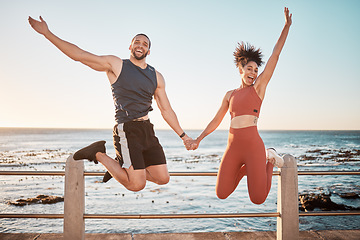 Image showing Fitness, energy and portrait of a couple jumping at beach for training fun, support and celebration of goal. Jump, happy and excited man and woman holding hands at the sea for cardio in Spain