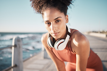 Image showing Portrait, fitness and black woman tired, ocean and runner with headphones, focus and determined for goal. African American lady, female exhausted and athlete with podcast, rest or training for health