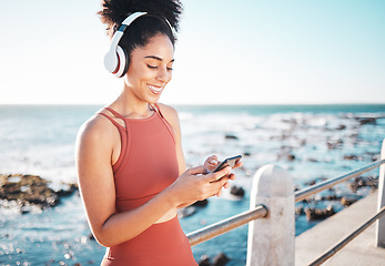 Image showing Black woman at beach, headphone and phone with fitness, runner listening to music for sports motivation. Happy, streaming online with podcast or radio, smartphone and running by sea with calm outdoor