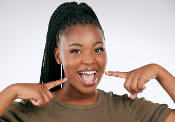 Image showing Portrait, dental and a black woman pointing to her mouth in studio on a gray background for oral hygiene. Face, teeth and an attractive young female inside to point at her teeth for whitening