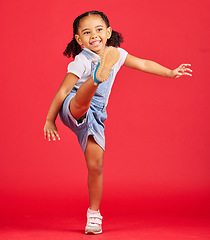 Image showing Happy, kick and excited girl in a studio with a casual, stylish and fashion kid outfit. Happiness, smile and young child with cool clothes kicking her leg with excitement isolated by a red background