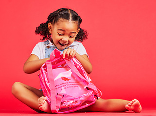 Image showing School, bag and red background with a student black girl in studio sitting on the floor against a wall. Children, education and excited with a female kid pupil getting ready for learning, or growth