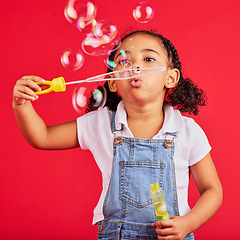 Image showing Little girl, playing or blowing bubbles on isolated red background in hand eye coordination, activity or fun game. Child, kid or youth with soap, wand or toy in studio for breathing development skill