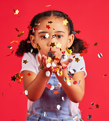 Image showing Young girl, kid blowing confetti with party and celebration, gold and glitter isolated against red background. Fun, youth and child at event, celebrate and birthday in studio with decoration