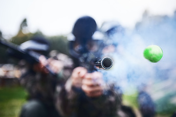 Image showing Paintball, shooting and person with a gun during a game, competition or match on a field. Fire, smoke and tool in motion for attack, battle and aim with a weapon during an outdoor cardio sport