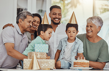 Image showing Birthday, celebration and twins blowing the candles on a cake at their party with family. Happy, excited and children with their parents and grandparents at event in a kitchen of a home to celebrate.