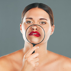 Image showing Portrait, magnifying glass and lips with a model woman in studio on a gray background for red makeup. Face, cosmetics or search with an attractive and funny young female checking her skin