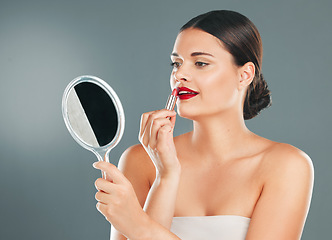 Image showing Lipstick, woman and mirror on studio background for beauty, fashion and aesthetics. Young model, red lips and makeup application with reflection for glamour cosmetics, elegant skincare or cosmetology