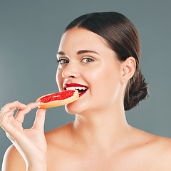 Image showing Fruit bite, portrait and woman eating a grapefruit for nature and wellness aesthetic in a studio. Model, beauty and natural skincare of a young person with red lipstick hungry for vitamin c nutrition