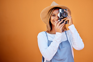 Image showing Photographer, portrait and woman shooting a picture or photo with a retro camera isolated in an orange background. Happy, studio and female taking creative shots or fashion photographs as photography