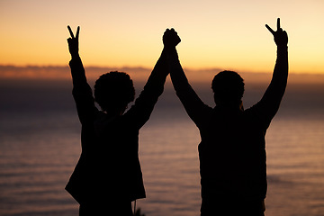 Image showing Sunset, beach and silhouette of couple celebration, success or winning and holding hands in shadow, night or dark. Sky, ocean and winner people in rear with peace sign for sea, hiking or travel goals