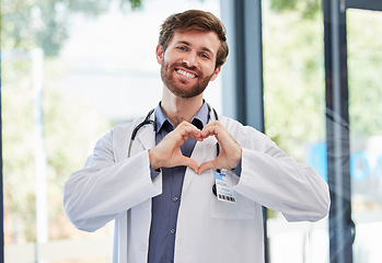 Image showing Doctor, man and heart hands with smile at hospital for support, cardiology or kindness by window. Medic portrait, hand sign or medical service with icon of care, love or help for consulting at clinic