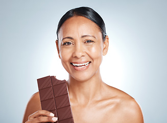 Image showing Candy, health and portrait of a woman with chocolate isolated on a blue background in studio. Food, happy and face of an elderly model showing a treat, sugar snack and sweets with smile on a backdrop