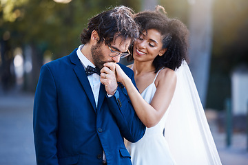 Image showing Wedding, happy couple and kiss on hand at marriage celebration event together with commitment. Interracial man and woman at ceremony with trust, partnership and care while outdoor with flower bouquet