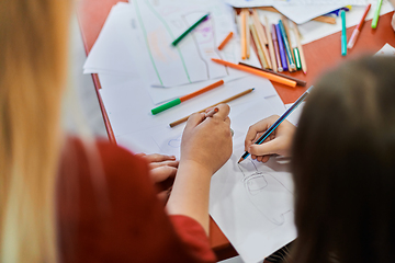 Image showing Close up photo of kids during an art class in a daycare center or elementary school classroom drawing with female teacher.