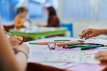 Image showing Close up photo of kids during an art class in a daycare center or elementary school classroom drawing with female teacher.