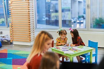 Image showing Creative kids during an art class in a daycare center or elementary school classroom drawing with female teacher.