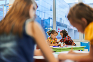 Image showing Creative kids during an art class in a daycare center or elementary school classroom drawing with female teacher.