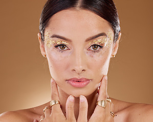 Image showing Gold makeup, woman jewelry and beauty portrait with model ready for luxury skincare and spa. Brown background, studio and isolated young female person with rings, vitiligo and glitter eyes alone