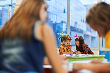 Image showing Creative kids during an art class in a daycare center or elementary school classroom drawing with female teacher.