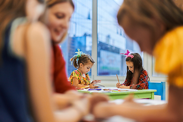 Image showing Creative kids during an art class in a daycare center or elementary school classroom drawing with female teacher.