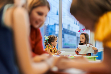 Image showing Creative kids during an art class in a daycare center or elementary school classroom drawing with female teacher.