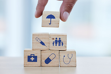 Image showing Hands, wood and building blocks on table for insurance, healthcare or a safe healthy foundation. Hand of doctor putting small wooden block, object or icons with umbrella to build medical investment